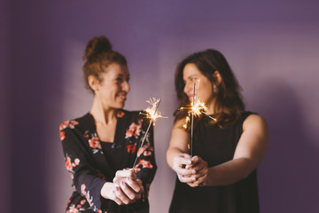 two young beautiful women having fun with sparkles indoors. Purple background. Casual clothing. Fun, happiness and lifestyle