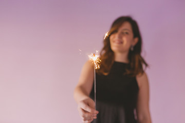 Obraz premium young beautiful woman having fun with sparkles indoors. Purple background. Casual clothing. Fun, happiness and lifestyle