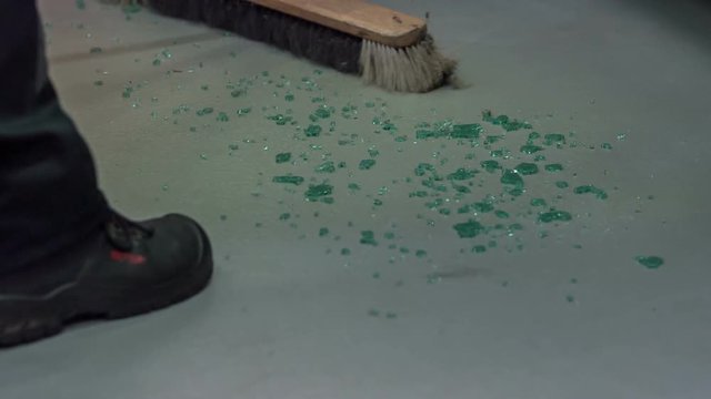 A glass has been broke and someone is slowly sweeping the floor to clean it up.