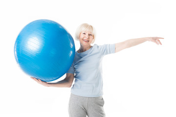 Smiling senior sportswoman holding fitness ball in one hand isolated on white