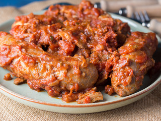 Sausages and pork pullet cooked in traditional Italian tomato ragu sauce. Dish on burlap with cutlery.