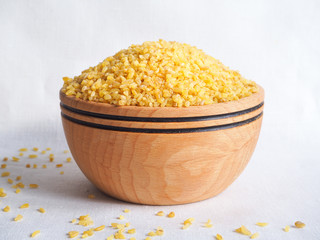 Dry bulgur wheat in wooden bowl. Spilled bulgur
