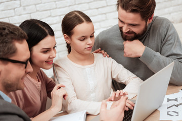 Bearded father and beautiful mother look at how little daughter prints on laptop at doctor office.