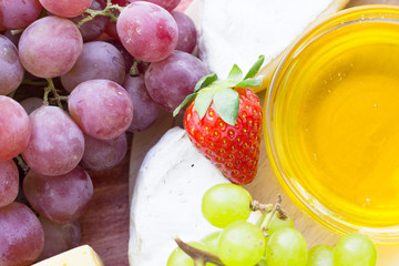 Snacks with wine - Strawberry, various types of cheeses, figs, nuts, honey, grapes on a red wooden background