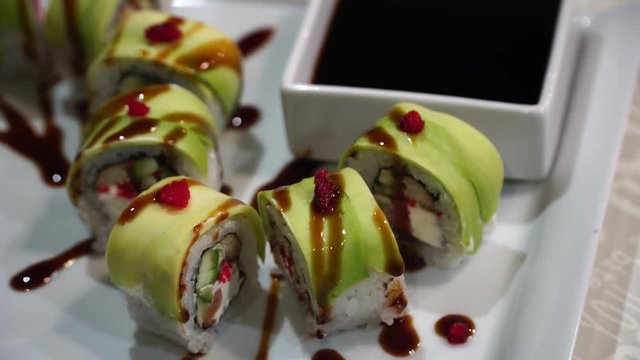 Close up green dragon roll and place it on a plate or platter set. Served in Japanese bar restaurant. Top view, flat lay. Food background. 4K