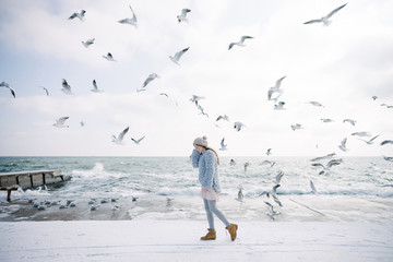 stylish young girl on winter seashore with seagulls