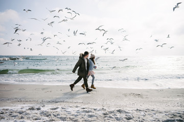 young couple running on winter sea shore with seagulls