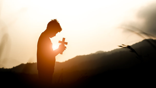 Young holding christian cross with light sunset background