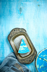 sliced cake and piece of mousse cake with blue glaze on a looking like silver, vintage metal dish on the white-blue wooden background