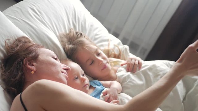 Happy mother and her young children taking selfie with smartphone on bed