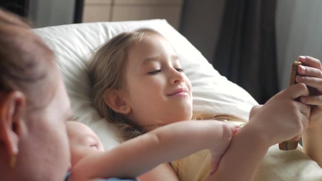 Happy mother and her young children taking selfie with smartphone on bed