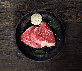 Fresh raw beef meat steaks in the black plate on black wooden background