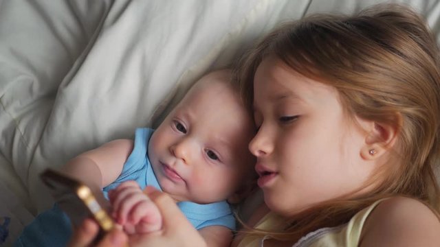 Little baby boy and girl playing with tablet computer on the bed