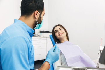 Obraz premium Dentist examining patient's teeth, good-looking man with black hair wearing blue uniform and gloves, looking at patient's teeth carefully with dental instruments
