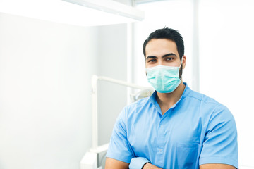 Fototapeta na wymiar Portrait of hadsome dentist doctor wears blue uniform and face mask, indoor shot in modern dentist office