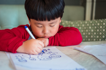 A Asian boy is drawing a picture.