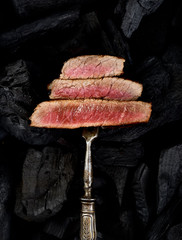 Slices of Medium rare grilled Steak Ribeye on meat fork on black background