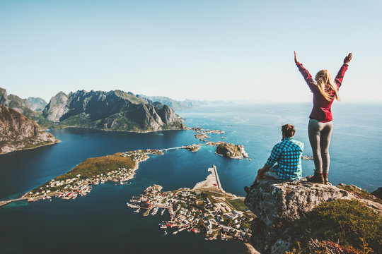 Couple family traveling together on cliff edge in Norway man and woman lifestyle concept summer vacations outdoor aerial view Lofoten islands Reinebringen mountain top