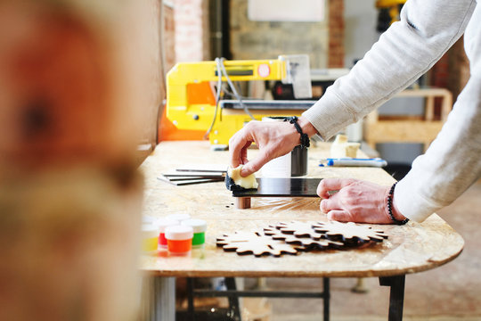 A young master paints a wooden piece in a handmade workshop