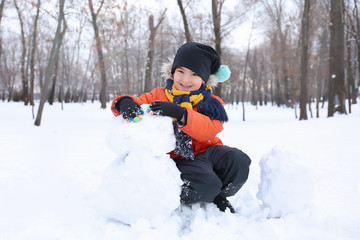 Fototapeta na wymiar Cute boy making snowman in park on winter vacation