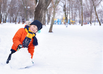 Cute boy making snowman in park on winter vacation