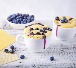 Cupcakes in a mug with berries / Vanilla cakes in a mug with blueberries on a white wooden background