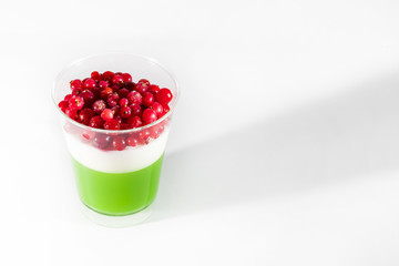 Creamy cream dessert in a plastic cup decorated with berries on a white background. 