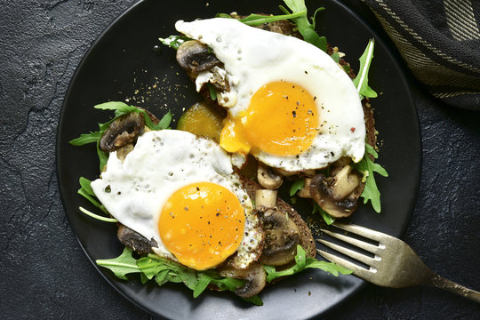 Whole grain toasts with sauteed mushrooms, fried eggs and arugula leaves.Top view with copy space.