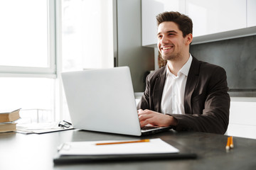 Cheerful young businessman using laptop computer.