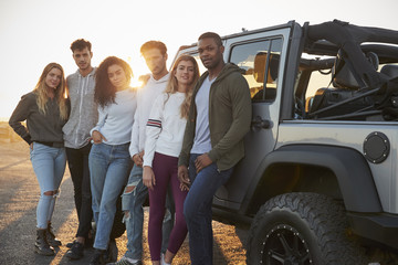 Young adult friends on a road trip standing by their jeep - obrazy, fototapety, plakaty