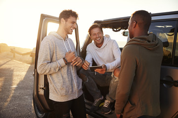 Three male friends on a road trip using a tablet computer - obrazy, fototapety, plakaty