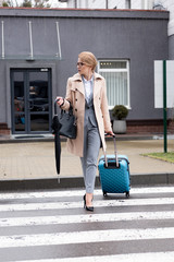 businesswoman with suitcase and umbrella crossing road on street