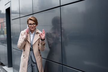 businesswoman showing ok sign while talking on smartphone on street