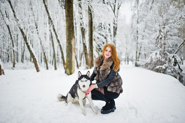 Naklejka na ściany i meble Red haired girl walking at park with husky dog on winter day.