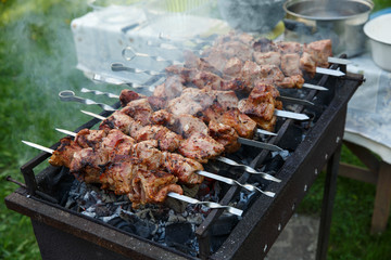 Shashlik or shashlyk preparing on a barbecue grill over charcoal. Grilled cubes of pork meat on metal skewer. Outdoor.