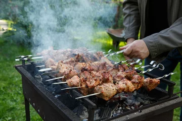  Shashlik or shashlyk preparing on a barbecue grill over charcoal. Grilled cubes of pork meat on metal skewer. Outdoor. © geshas