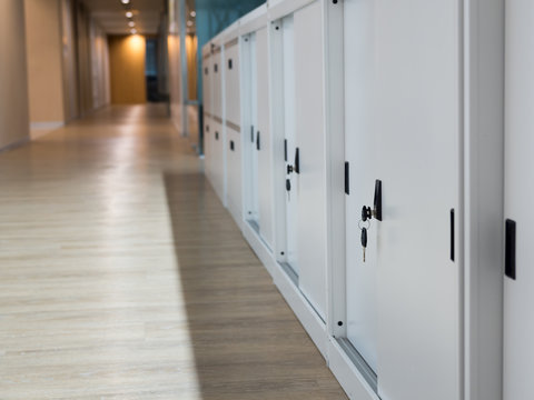 Select focus for key. White Cabinet for document storage. The keys are plugged into the filing cabinet. The filing cabinet is located on the floor beside the walkway.