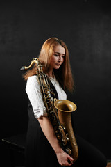 Young woman with saxophone on black background