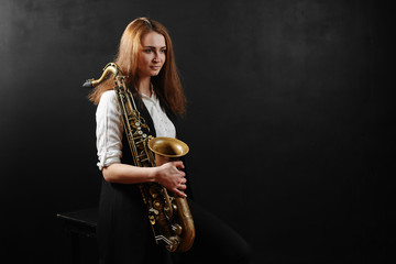 Young woman with saxophone on black background