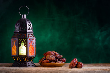 Ramadan concept. Dates close-up in the foreground. Ramadan Lantern on a wooden table. Textured green wall background. Space for text on the right.