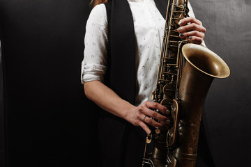 Young woman with saxophone on black background