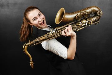 Young woman with saxophone on black background