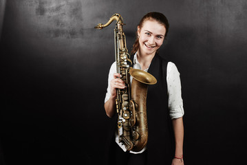 Plakat Young woman with saxophone on black background