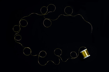 Spool of gold thread on a black background.