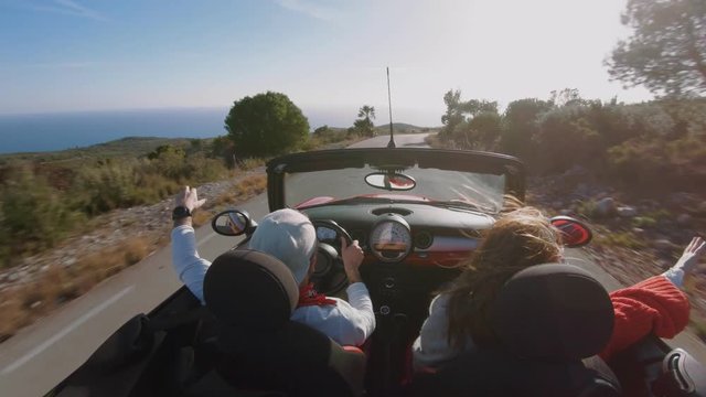 Amazing and casual coupe of hipsters or millennials, man and woman enjoy convertible cabriolet ride in slow motion, catch wind with hands and hair on sunset evening road, travel inspiration