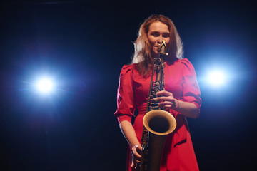 Musician girl in a red dress with a saxophone on stage