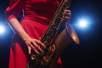 Obraz premium Musician girl in a red dress with a saxophone on stage