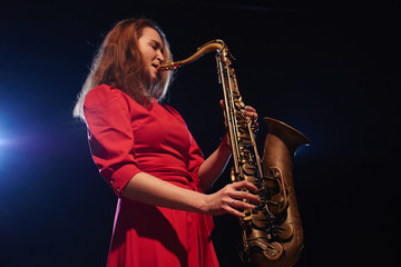 Fototapeta na wymiar Musician girl in a red dress with a saxophone on stage
