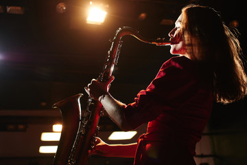 Musician girl in a red dress with a saxophone on stage