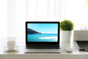 Beach in screen Laptop on table and Coffee cup room Office morning.concept of time relax.